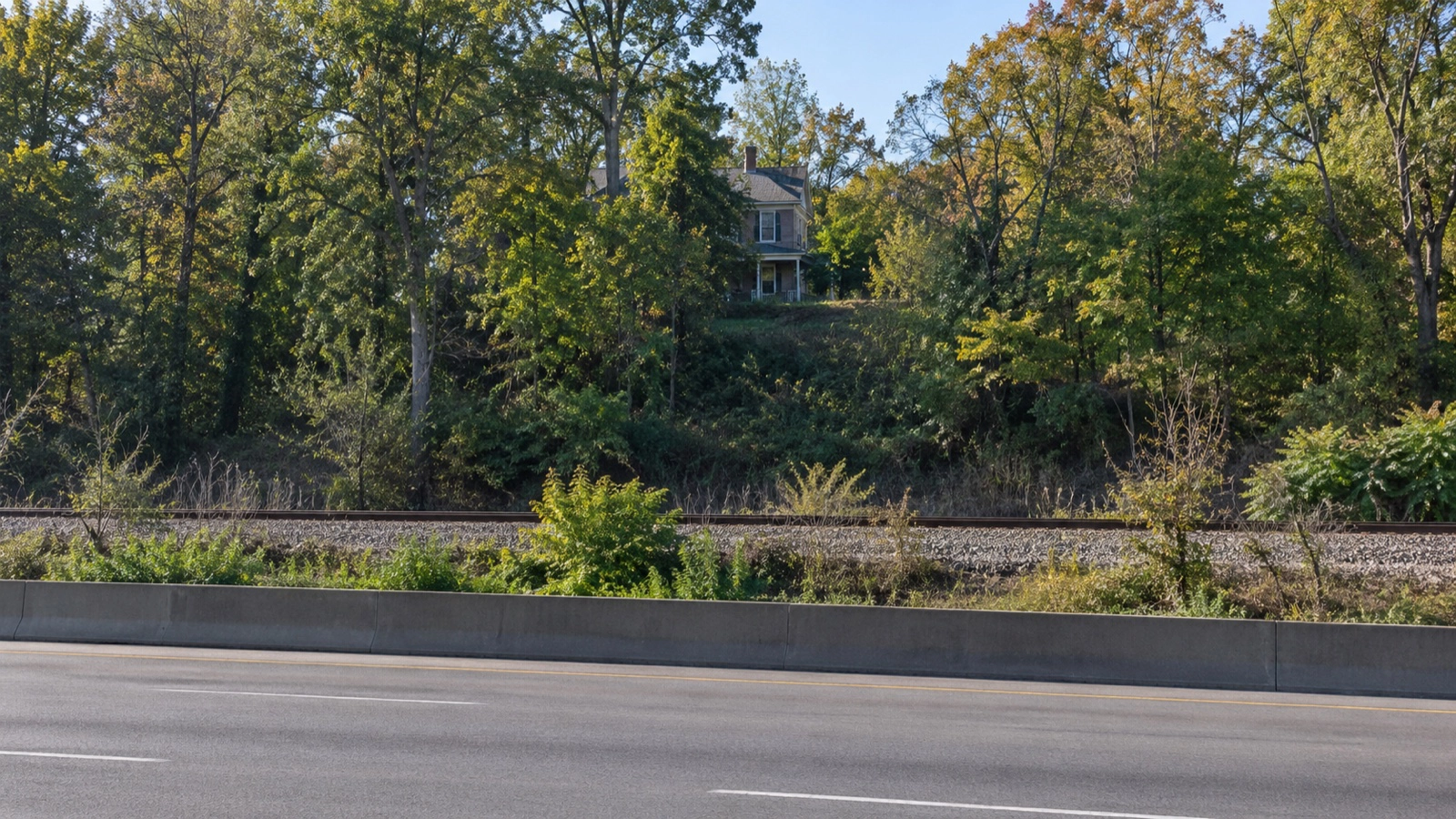 Unidentified older house viewed at a distance beyond a highway and railroad tracks